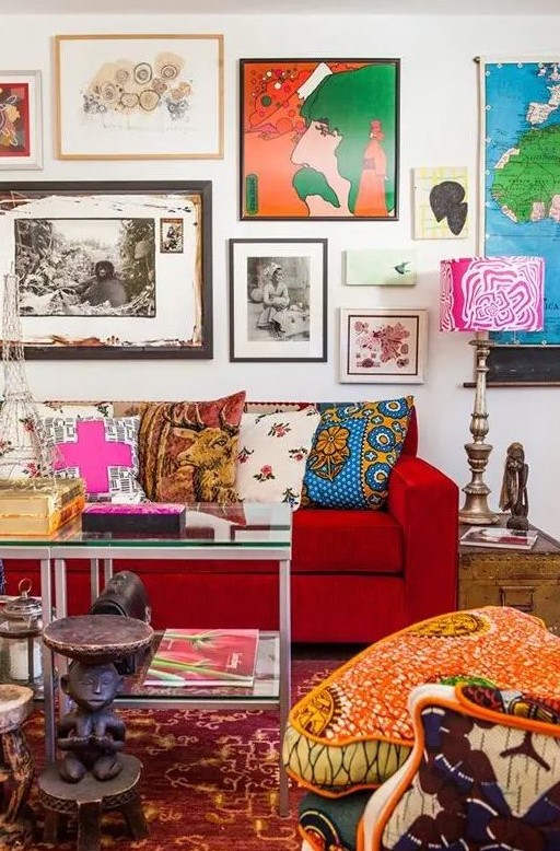 a maximalist living room with a colorful gallery wall, a hot red sofa, a printed chair, a bright rug and some pillows and books