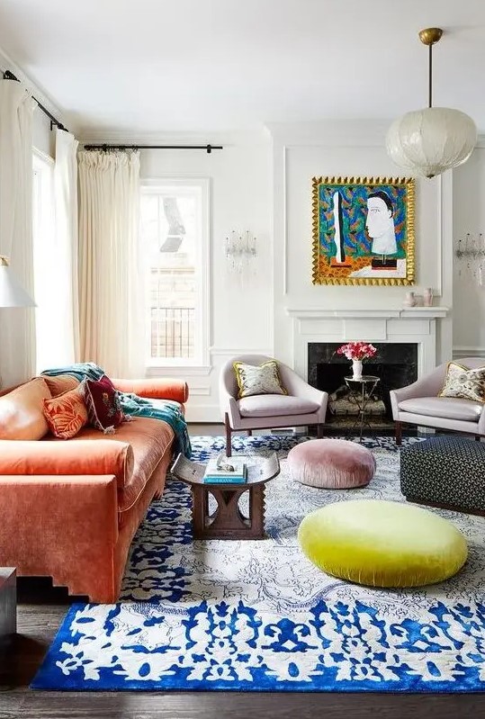 a maximalist living room with a coral sofa, a bold blue rug, pastel ottomans, lilac chairs and a bold artwork