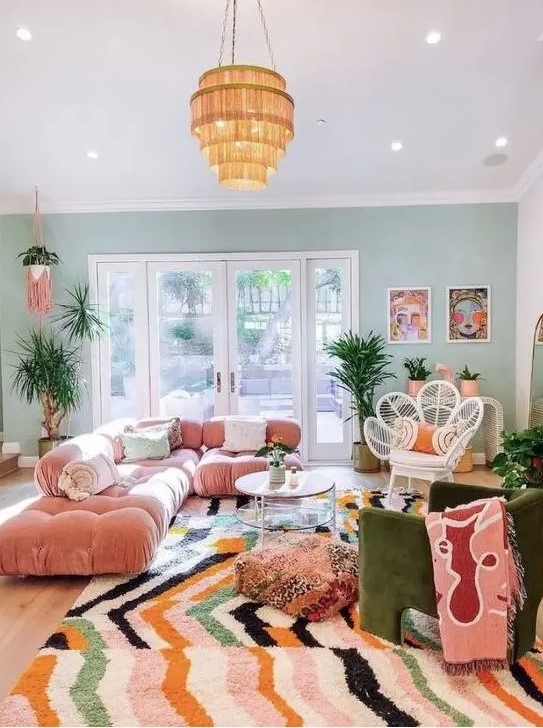 a maximalist living room with a green accent wall, a pink sofa, a green chair, a bright rug and a glazed tiered table