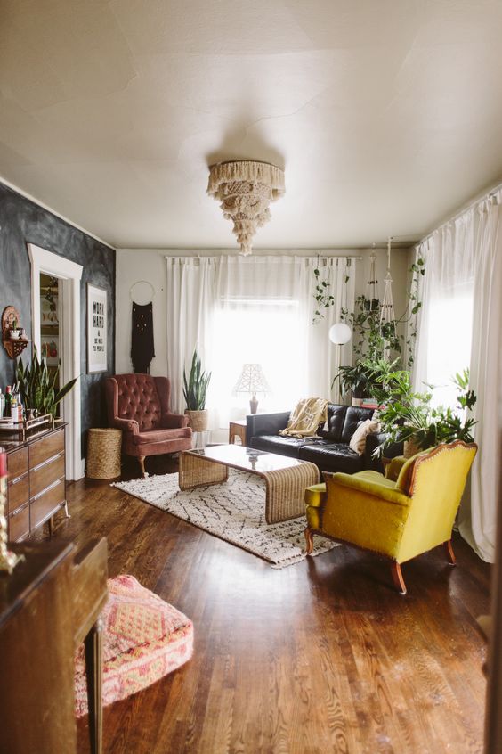 a modern eclectic and boho living room with a black leather sofa, a mustard and burgundy chair, potted greenery and some cool decor