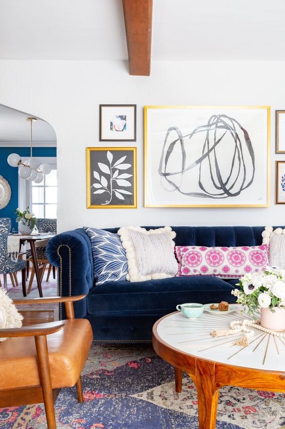 a modern eclectic living room with a navy sofa, amber chairs, a round coffee table, colorful pillows, a free form gallery wall