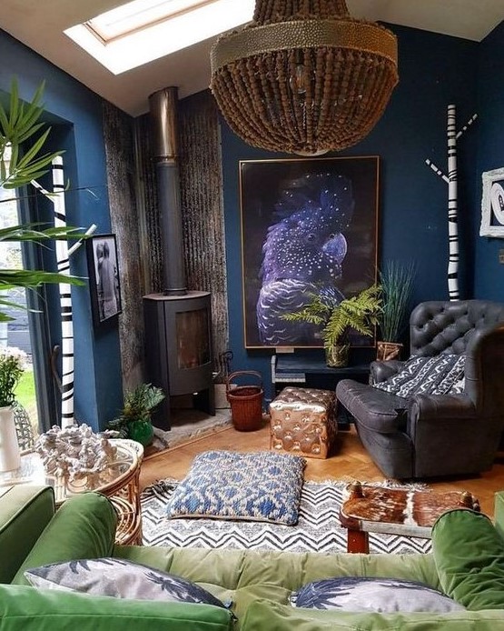 a moody eclectic living room with navy walls, black and green furniture, a bead chandelier and a vintage hearth