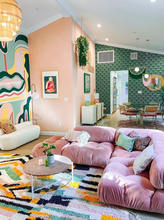 a pretty eclectic living room with coral walls, a bold accent rug, a pink sofa, a coffee table and a bold rug