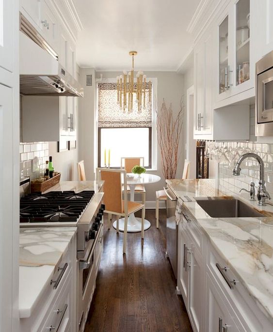 A Small And Welcoming Galley Kitchen With White Cabinets And White Stone Countertops A Cozy Dining Space Wth A Round Table And A Glam Chandelier 