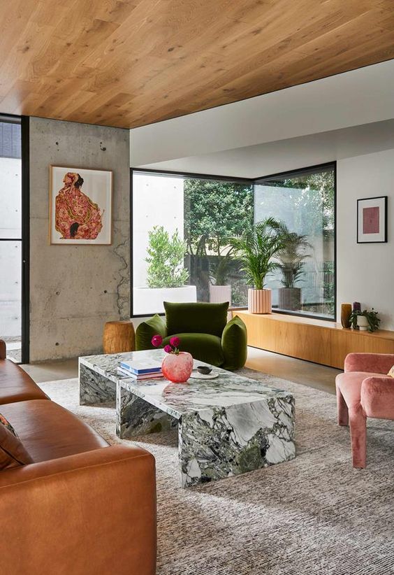 an eclectic living room with concrete walls and a stained ceiling, a leather sofa, marble tables and a dark green chair