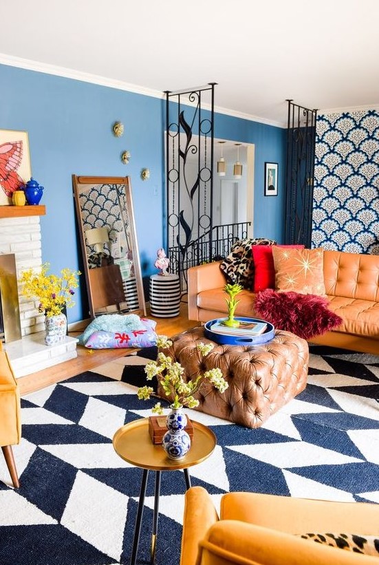 bright maximalist living room with blue walls, a chevron rug, an amber sofa and an ottoman, yellow chairs, a gold table and a fireplace