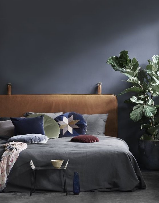 a moody bedroom in black refreshed with a potted plant, bright pillows and a leather hanging headboard for a statement