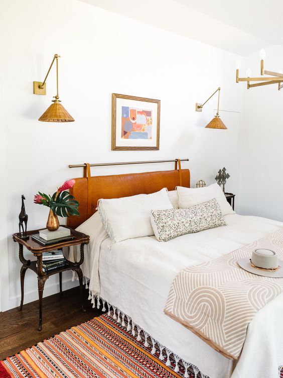 a neutral boho bedroom with a bed and an amber suspended headboard, neutral bedding, a bold rug and vintage nightstands, woven sconces