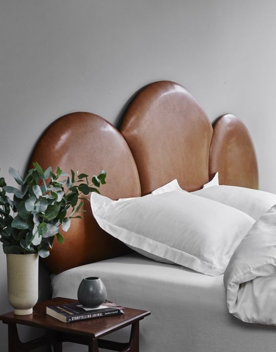 a refined bedroom with a cloud-shaped leather headboard, neutral bedding, a nightstand with greenery and decor