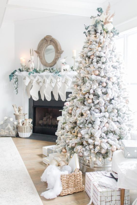 https://www.digsdigs.com/photos/2019/11/03-a-neutral-living-room-with-a-flocked-Christmas-tree-with-metallic-ornaments-a-basket-with-gifts-white-stockings-with-monogram-greenery-and-baskets-with-firewood.jpg