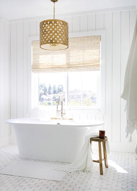 a-chic-white-bathroom-with-shiplap-walls-a-mosaic-tile-floor-a-tub-by-the-window-and-a-fabric-covered-vanity.jpg