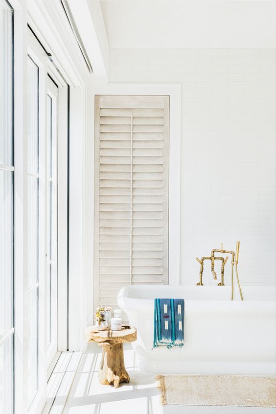 a-light-filled-white-bathroom-with-a-free-standing-tub-brass-fixtures-a-wooden-stool-and-a-glazed-wall-plus-shutters.jpg