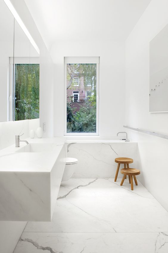 بالصور ديكورات حمامات انيقة باللون الابيض لمنزلك في ربيع 2020 حصري A-minimalist-white-bathroom-done-with-marble-a-floating-sink-and-marble-clad-tub-plus-a-window