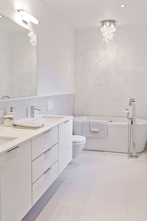 بالصور ديكورات حمامات انيقة باللون الابيض لمنزلك في ربيع 2020 حصري A-refined-white-bathroom-clad-with-tiles-of-various-sizes-with-a-chic-chandelier-and-a-large-white-vanity