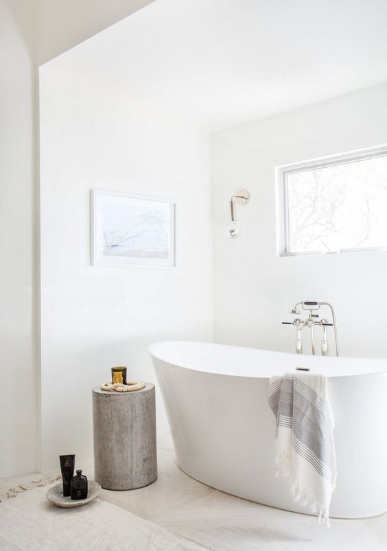 بالصور ديكورات حمامات انيقة باللون الابيض لمنزلك في ربيع 2020 حصري A-serene-white-bathroom-with-marble-tiles-on-the-floor-a-tub-a-wooden-stool-a-window-and-some-wall-sconces