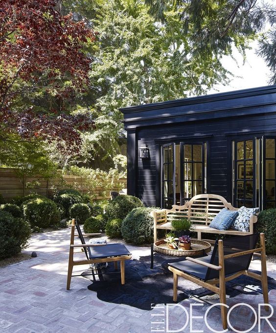 a small and elegant patio with a woven table and wooden seating furniture, greenery around is a very cool space