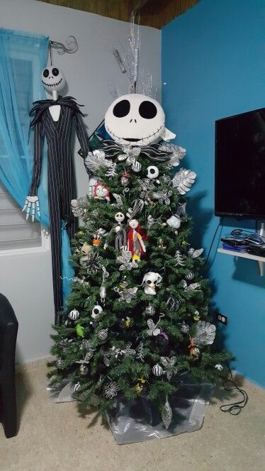 A holiday tree adorned with Nightmare Before Christmas decorations and with Jack Skellington standing beside it.