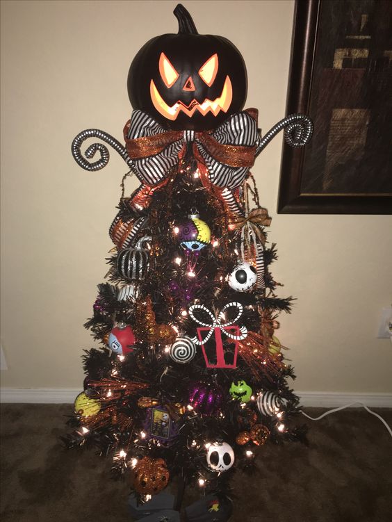 A dark Halloween or Christmas tree adorned with Nightmare Before Christmas decorations, fairy lights, a ribbon, and a massive pumpkin.