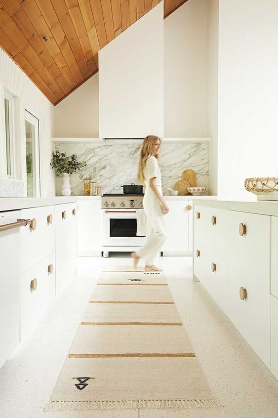 مطبخ أبيض هادئ مع خزانات رائعة ومقابض خشبية وغطاء أبيض متناسق لا يختلف عنهم على الإطلاق