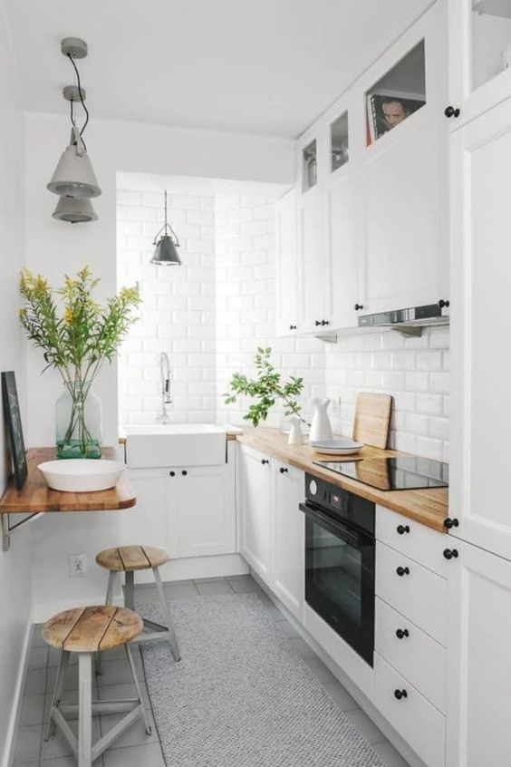مطبخ أبيض صغير ومريح مع شفاط مدمج وأغطية بوتشربلوك وأجهزة مدمجة بالإضافة إلى منطقة وجبات صغيرة