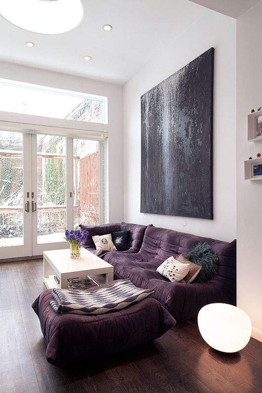 https://www.digsdigs.com/photos/2021/04/a-bold-modern-living-room-with-a-low-purple-sofa-and-a-large-pouf-a-white-table-and-an-oversized-black-artwork.jpg