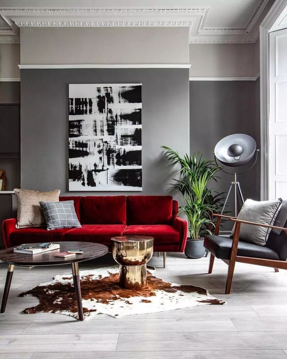 A Modern Living Room With Grey Walls A Bold Red Sofa A Black Leather Chair A Monochromatic Artwork And A Round Table 
