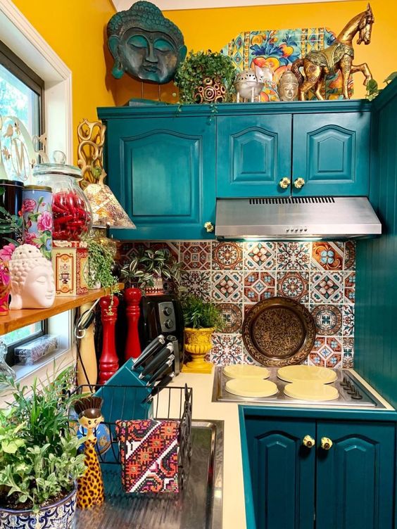 مطبخ ملون للغاية مع جدران بلون الخردل وخزائن زرقاء وبلاط ملون على باكسبلاش والكثير من الملحقات ونباتات الأصص