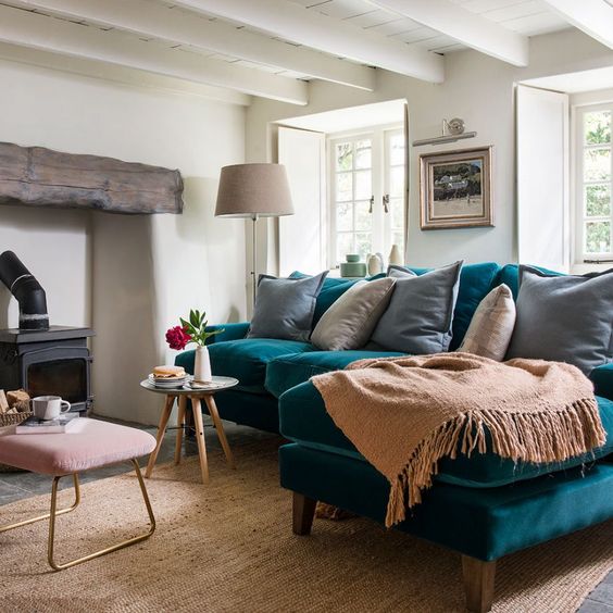 https://www.digsdigs.com/photos/2021/05/a-lovely-living-room-with-a-hearth-with-a-wooden-beam-a-turquoise-sofa-neutral-textiles-a-pink-ottoman-and-a-vintage-lamp.jpg