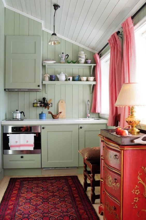 مطبخ جميل للغاية بجدران زيتون خضراء ومطبخ وخزانة حمراء وكرسي أنيق وستائر وردية وسجادة مشرقة