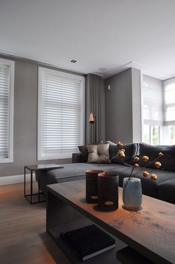 a contemporary taupe living room with a dark grey sofa, a wooden coffee table and a stone side table, a tan pillow and a copper lamp