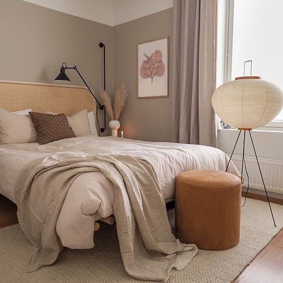 A Boho Taupe Bedroom With A Rattan Bed Neutral Bedding An Orange Leather Stool A Floor Lamp And Some Art And Pampas Grass 
