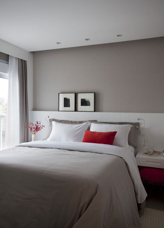 غرفة نوم صغيرة جميلة بجدار رمادي داكن ، وسرير مع لوح أمامي أبيض ممتد ، وطاولات جانبية عائمة ولمسات من اللون الأحمر