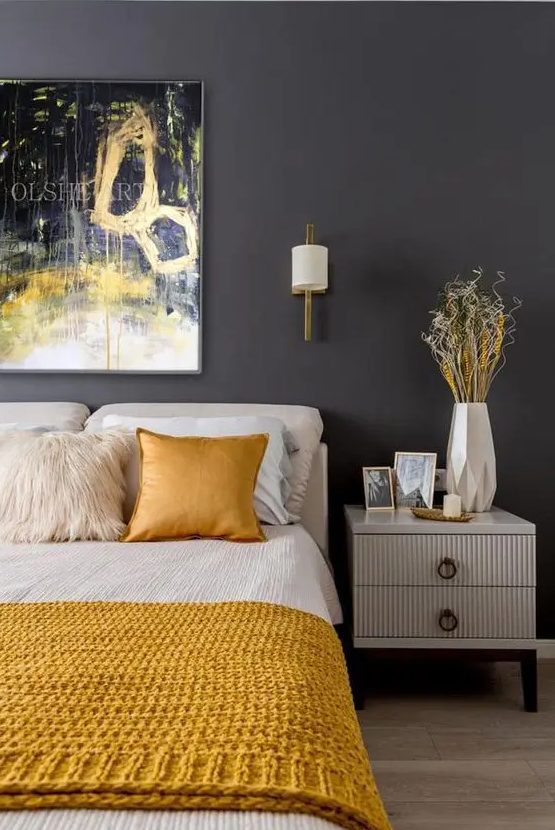 غرفة نوم جريئة بجدار رمادي جرافيت وأثاث كريمي وأسرّة كريمية وأصفر وعمل فني جريء فوق السرير