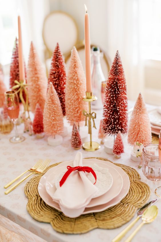 طاولة عطلة جريئة مع أشجار فرشاة الزجاجة باللونين الأحمر والوردي ، والشموع الوردية ، والمفارش المنسوجة والبورسلين الوردي