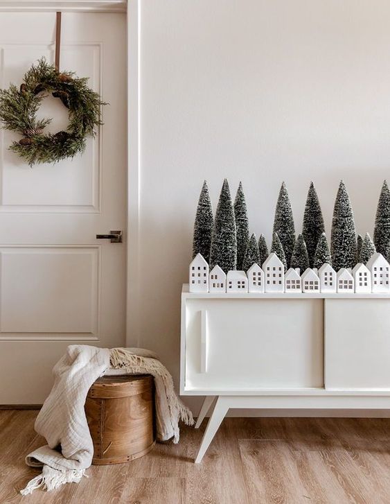 كردينزا أنيقة مع أشجار فرشاة الزجاجة وبيوت بيضاء صغيرة لديكور عيد الميلاد الاسكندنافي