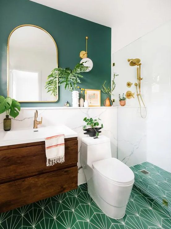 حمام حديث أنيق بجدار أخضر وأرضية من بلاط الفسيفساء الأخضر ، ومنضدة زخرفية ملونة ، ومرآة مقوسة ونباتات أصص.