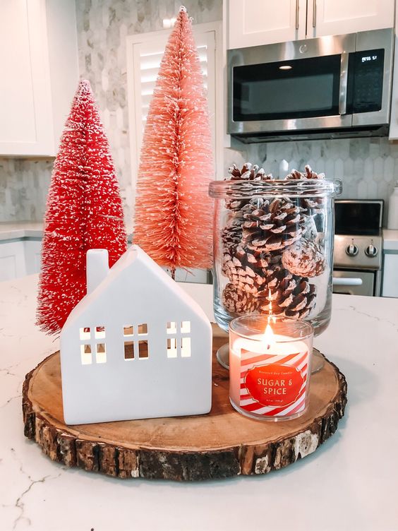 ترتيب عيد الميلاد الصغير لمنزل صغير ، جرة بها أكواز صنوبر ثلجية ، شمعة ، فرشاة زجاجة وردية وحمراء ، أشجار عيد الميلاد