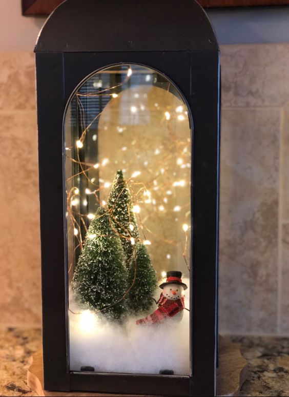 https://www.digsdigs.com/photos/2021/12/37-a-black-metal-lantern-with-faux-snow-bottle-brush-Christmas-trees-lights-and-a-small-snowman-is-a-lovely-idea.jpg
