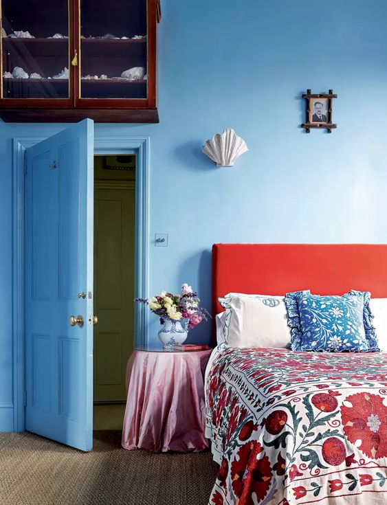 غرفة نوم زرقاء جميلة مع سرير coquelicot وفراش مطبوع مشرق مع نفس الظلال ، ومنضدة كلاسيكية مع أزهار