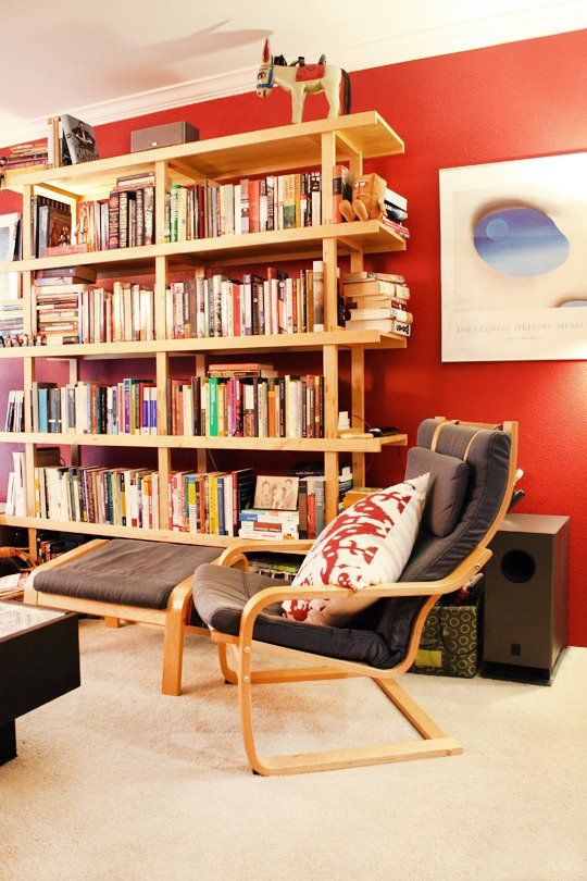 غرفة جلوس جريئة مع جدار لهجة coquelicot ، خزانة كبيرة مفتوحة ، كرسي رمادي مع مسند للقدمين ، عمل فني مذهل