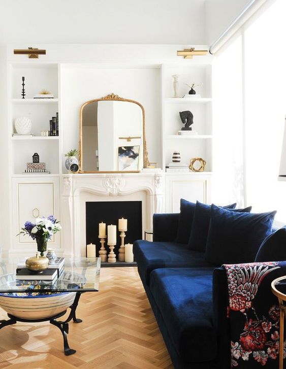 كنب عصري باللون الازرق A-beautiful-neutral-living-room-with-a-candle-fireplace-a-navy-sofa-built-in-shelves-a-glass-coffee-table-and-lovely-gold-touches-here-and-there