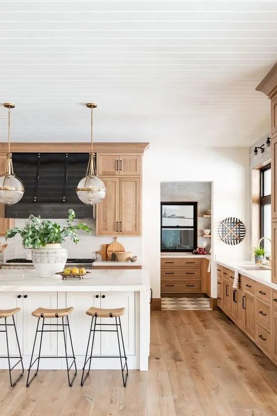 A Chic Modern Country Kitchen With Light Stained Cabinets And Hardwood Floors A White Kitchen Island Tall Stools And Pendant Lamps 