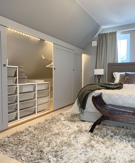 https://www.digsdigs.com/photos/2022/03/a-cozy-and-welcoming-neutral-bedroom-with-an-attic-space-taken-for-storage-clear-boxes-on-stand-and-a-holder-for-clothes.jpg