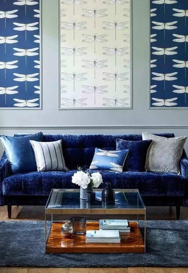 كنب مودرن باللون الازرق عصري وانيق A-living-room-with-an-electric-blue-sofa-printed-pillows-a-gallery-wall-of-wallpaper-a-tiered-coffee-table-and-a-midnight-blue-rug