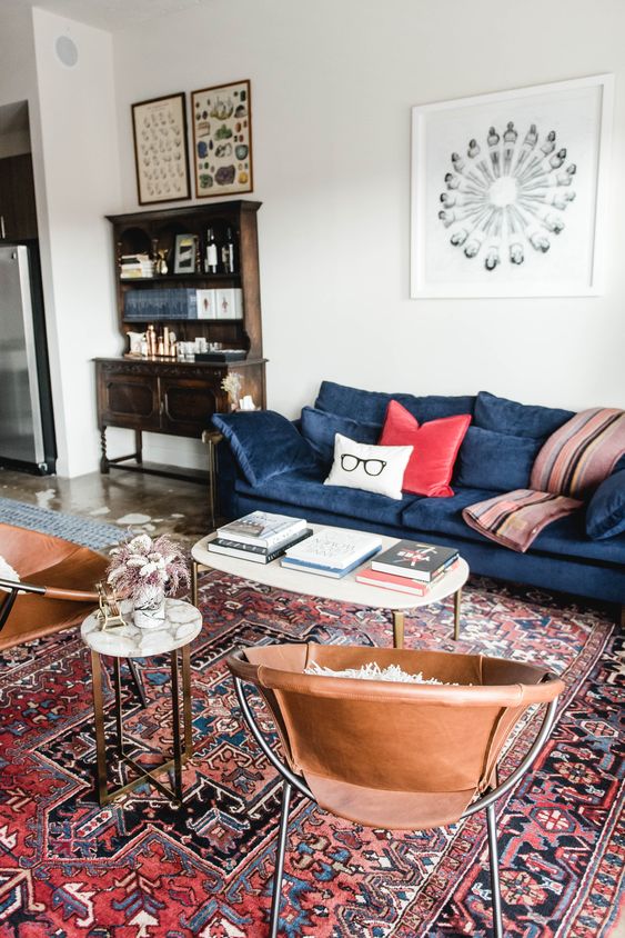كنب مودرن باللون الازرق عصري وانيق A-mid-century-modern-living-room-wiht-a-vintage-bureau-a-blue-sofa-with-colorful-pillows-leather-chairs-coffee-tables-and-a-red-printed-rug