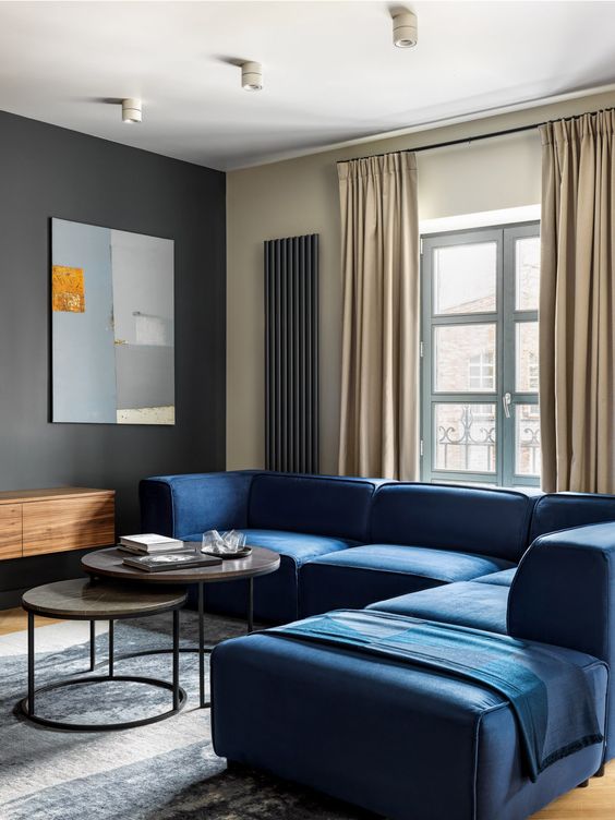 كنب مودرن باللون الازرق عصري وانيق A-minimalist-living-room-with-a-black-accent-wall-a-navy-sofa-round-tables-a-floating-credenza-neutral-curtains-and-a-pretty-artwork