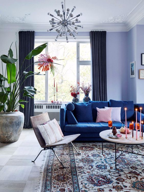 كنب مودرن باللون الازرق عصري وانيق A-pretty-living-room-done-with-a-cold-color-scheme-with-lilac-walls-a-navy-sofa-a-round-table-a-lovely-chair-some-greenery-and-a-sunburst-chandelier