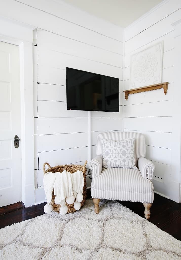 https://www.digsdigs.com/photos/2022/04/17-a-neutral-farmhouse-living-room-with-white-shipalp-walls-a-striped-vintage-chair-a-printed-pillow-a-basket-with-a-pompom-blanket-TV-cords-hidden-in-a-large-wire-tube-attached-to-the-wall.jpg
