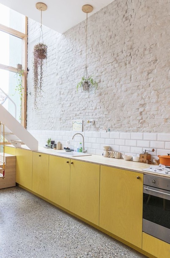 https://www.digsdigs.com/photos/2023/02/52-a-bold-contemporary-kitchen-with-yellow-plywood-cabinets-neutral-countertops-a-white-subway-tile-backsplash-and-a-brick-wall.jpg