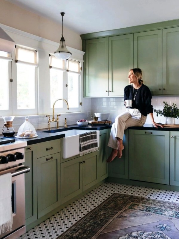 A Farmhouse Kitchen In Sage Green With Shaker Cabinets Black Countertops A White Subway Tile Backsplash And Brass Handles 